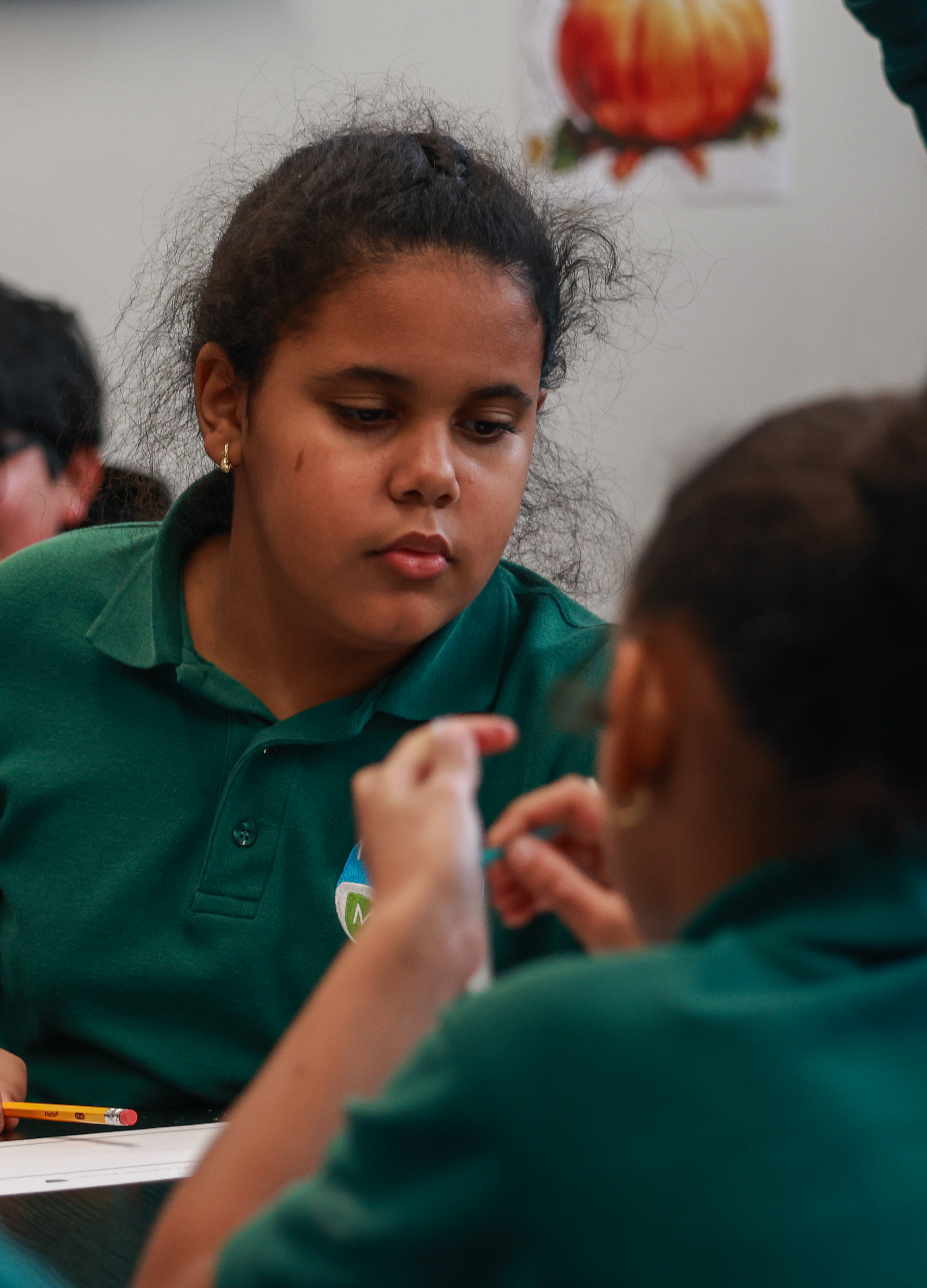 Photo of Alanis in a green school-uniform polo shirt, viewed over the shoulder of another student.