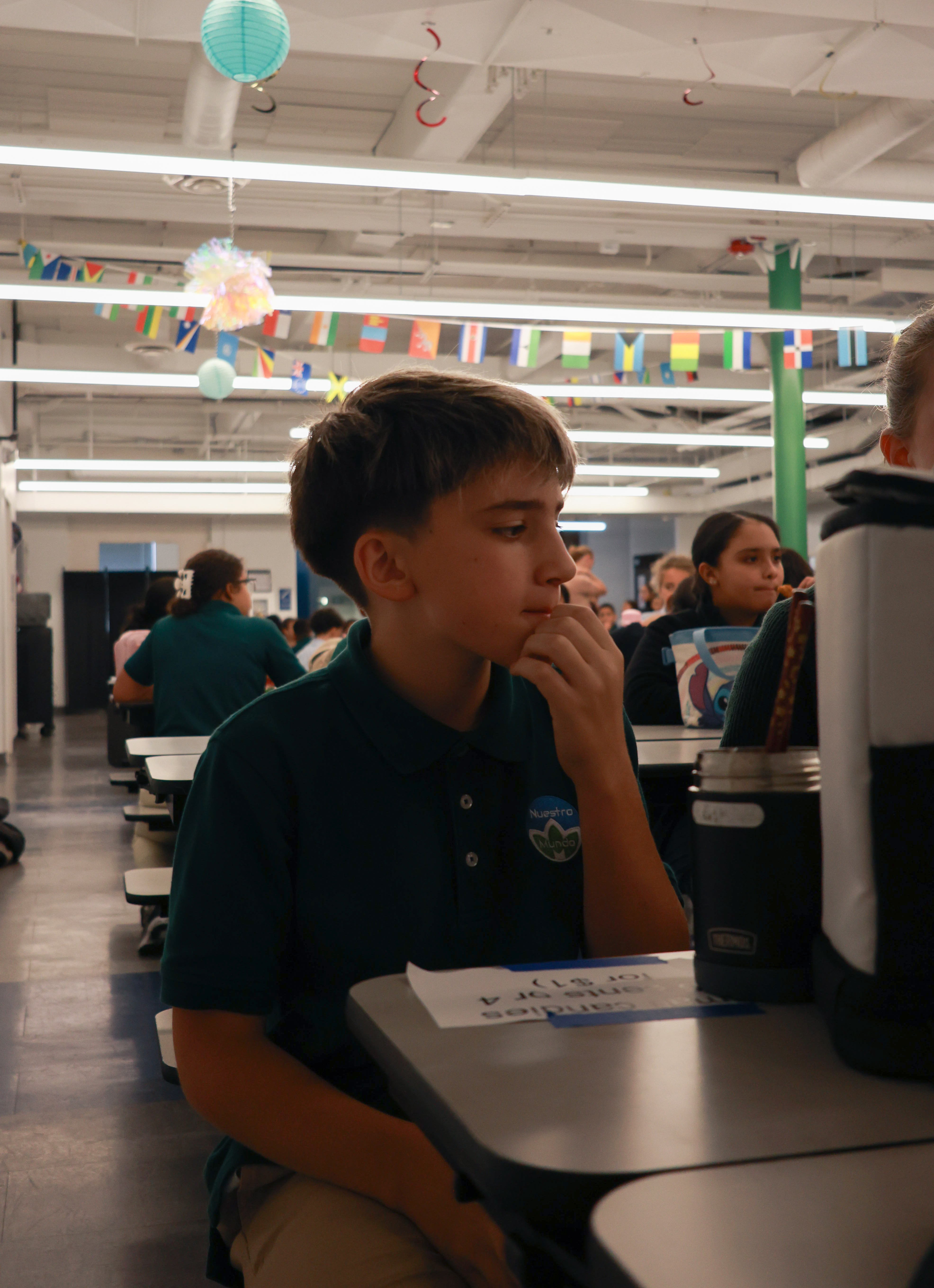 Beckham Gibb sits at a cafeteria table under banners displaying flags from around the world.
