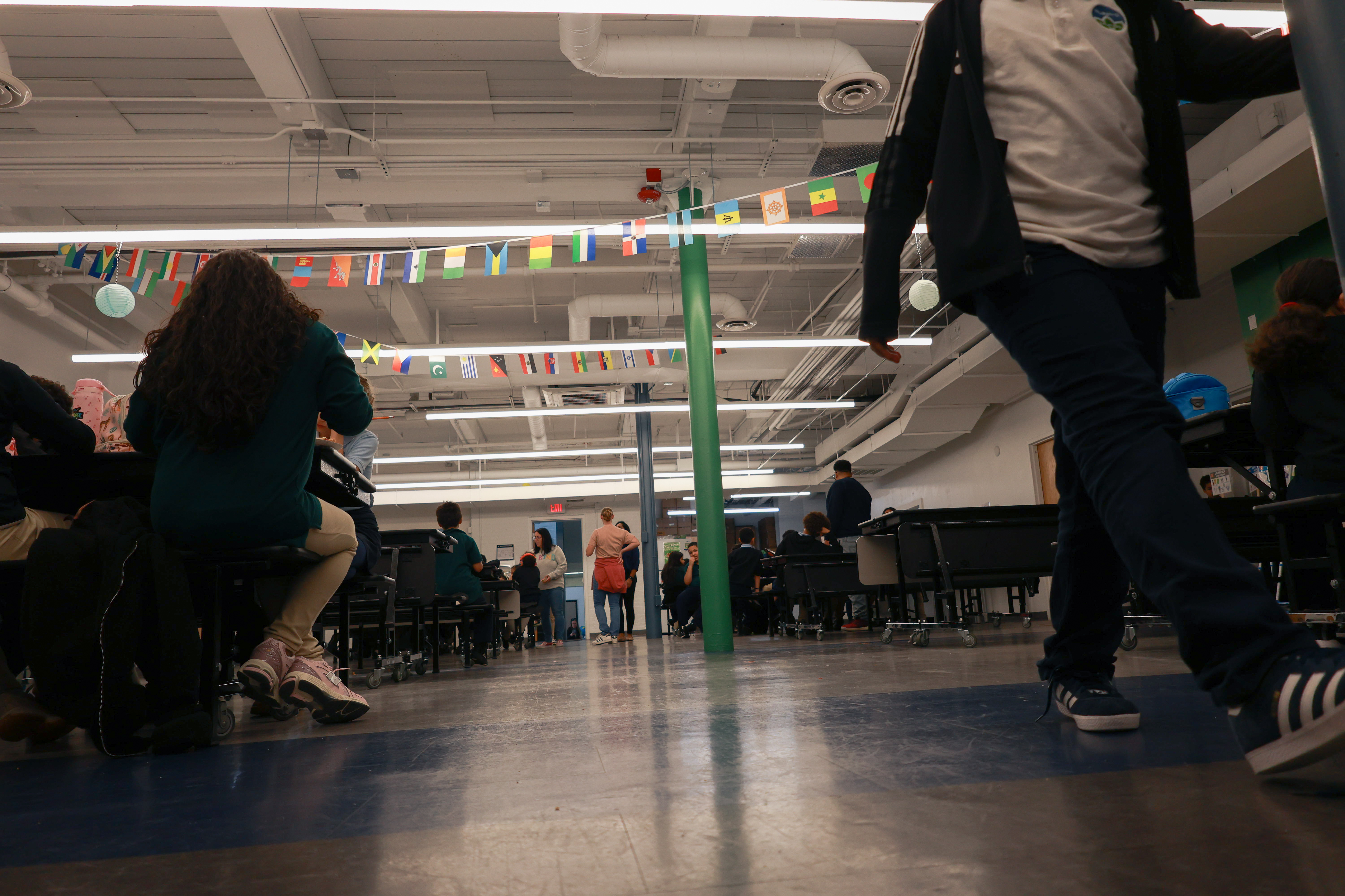 Photo of a student's legs walking through a cafeteria, filled with long tables and banners of flags from around the world.