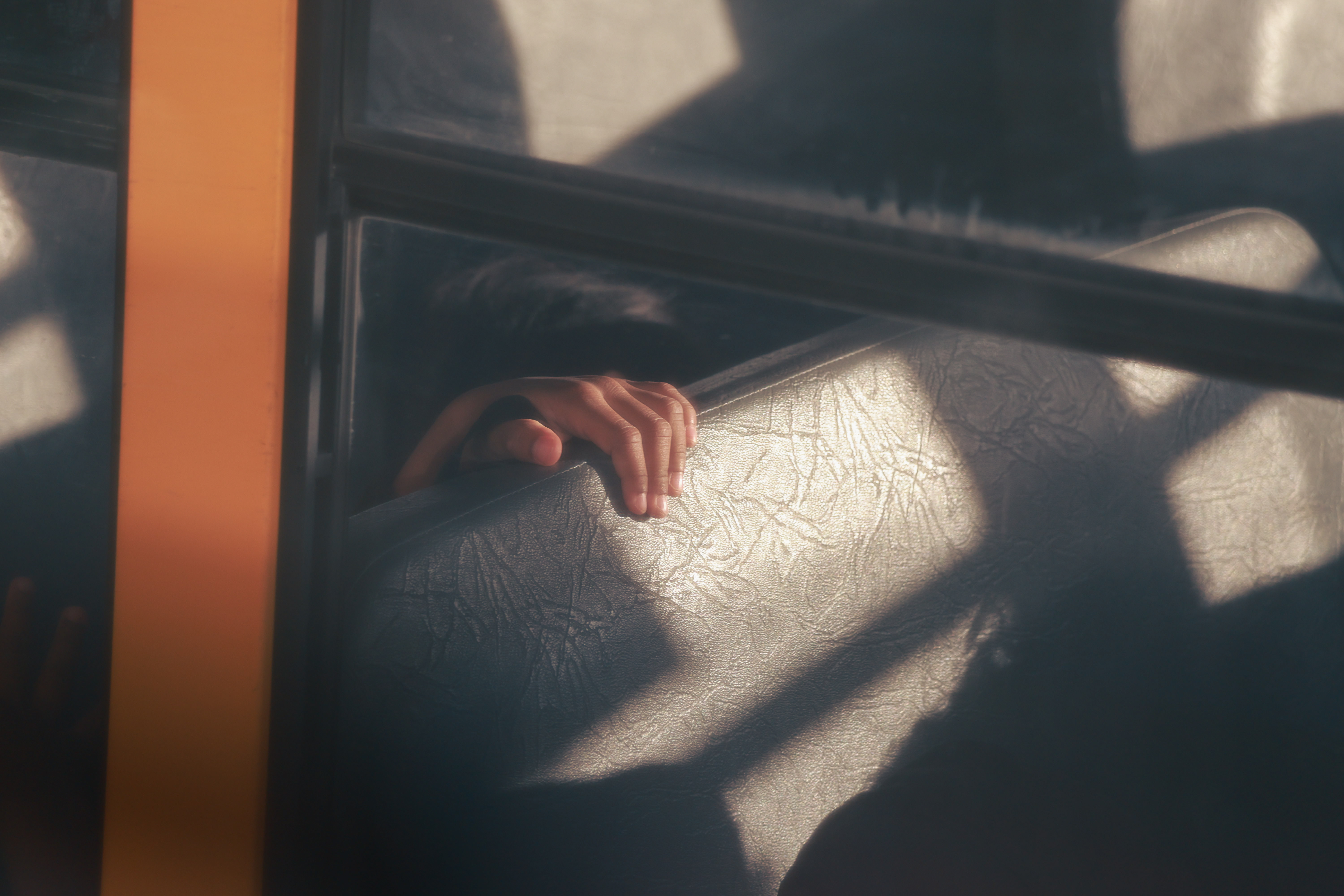 Photo of a child's hand, illuminated by a bright ray of sun, reaching over the back of a seat on a school bus.