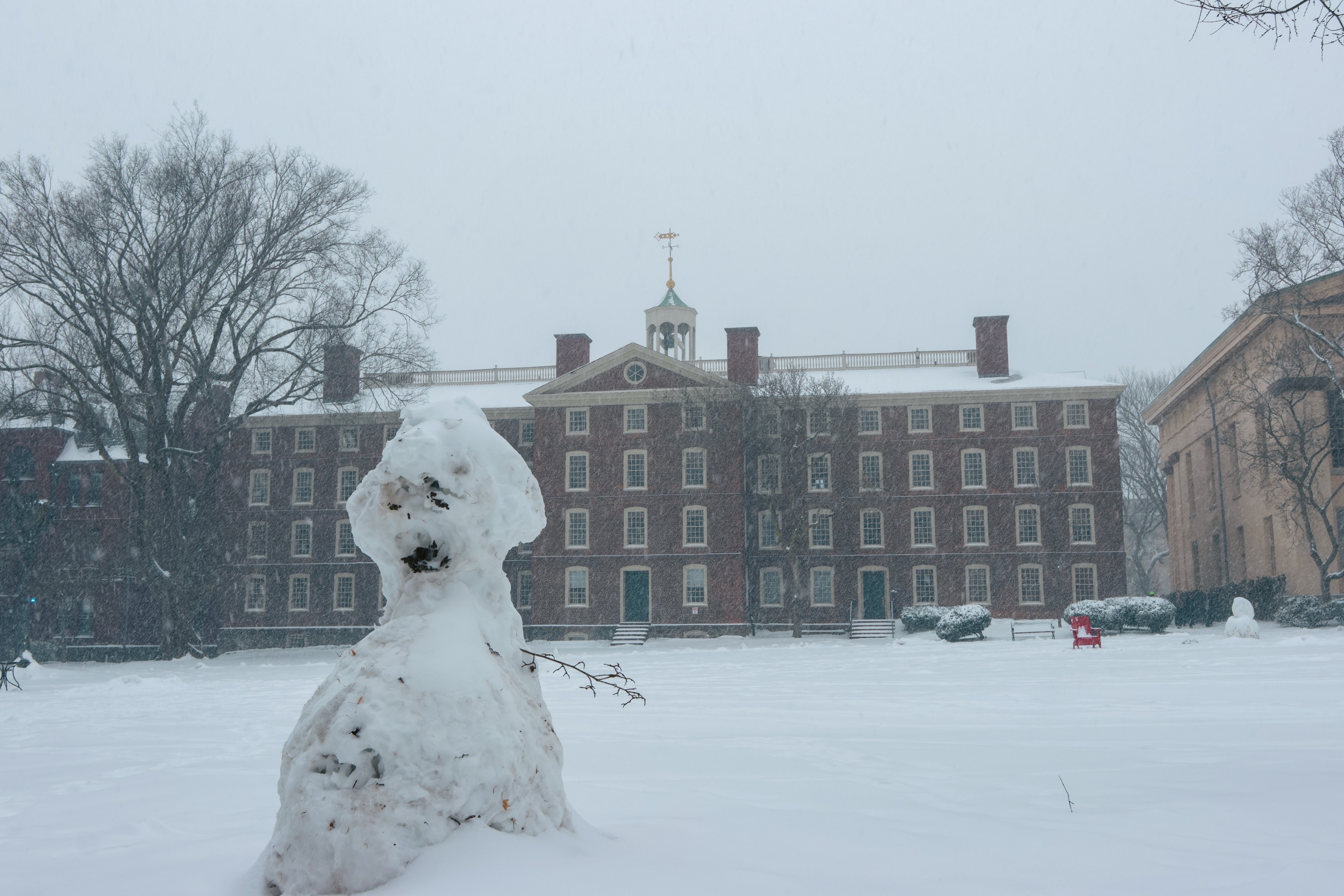 Photo of snowman in front of University Hall, with one stick arm on its left.