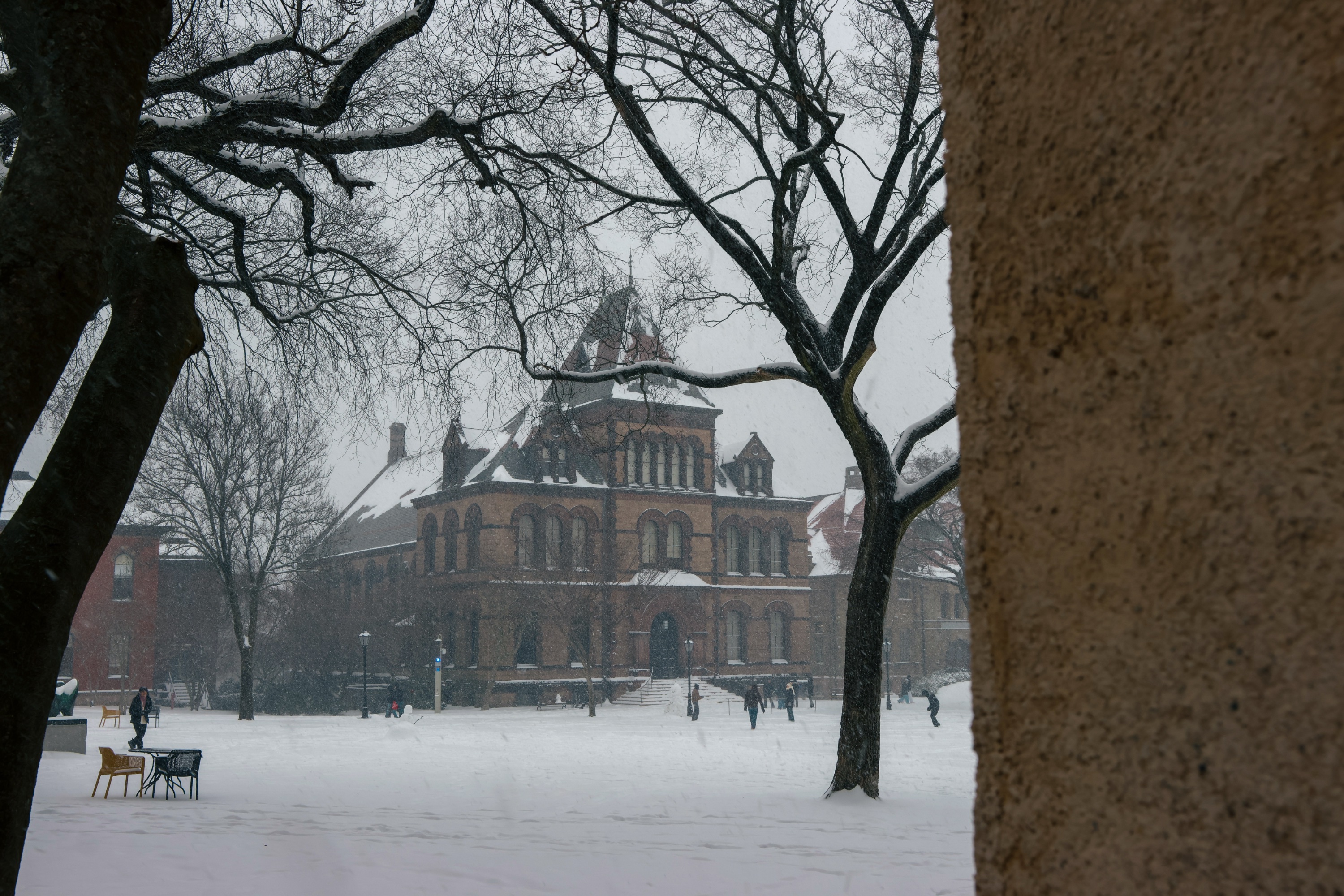 Photo of the Main Green covered in snow with the wall of a tan-colored building blocking the full scene. 