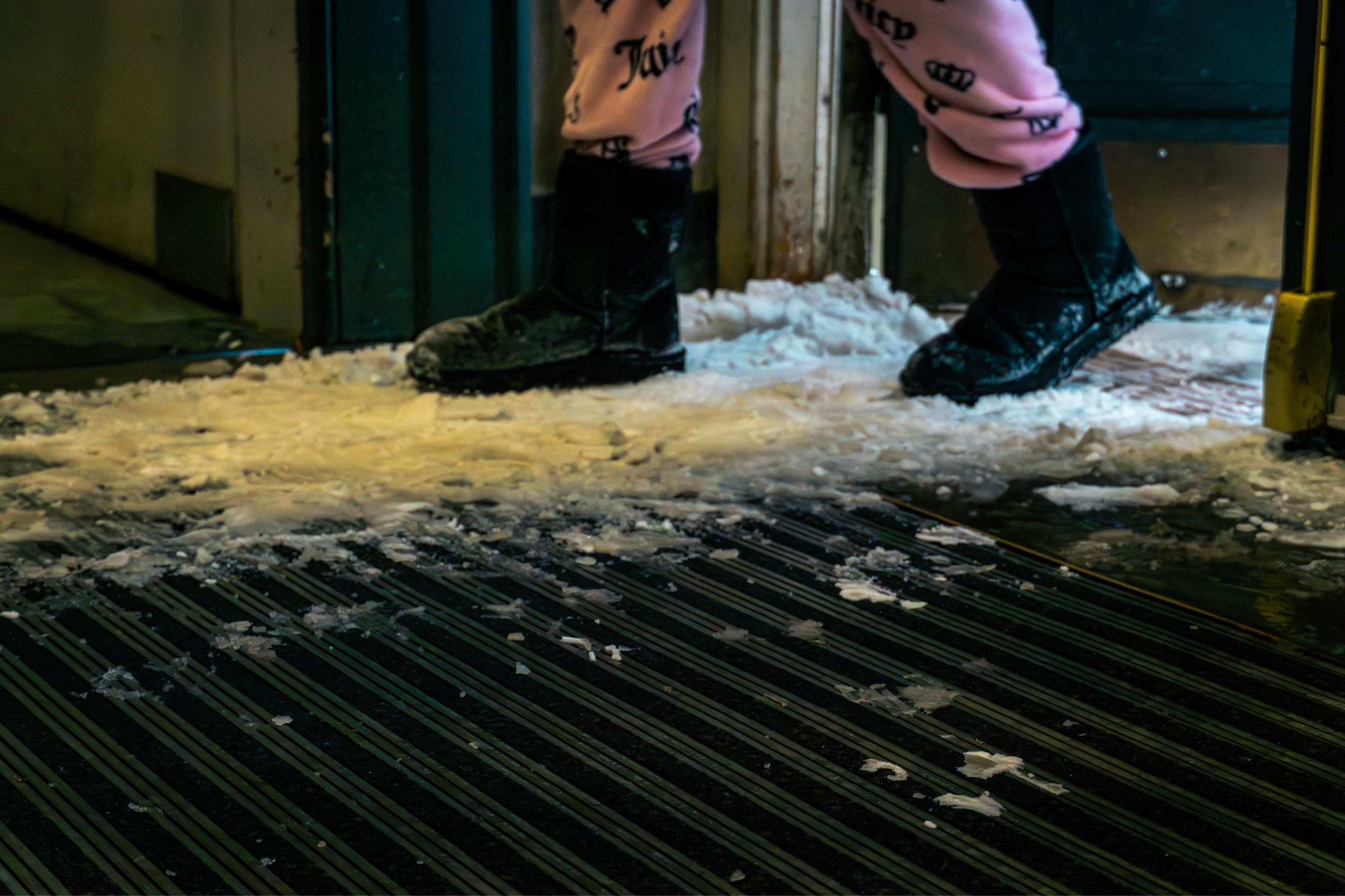 Photo of a person with pink fuzzy pants and black boots stepping through a door onto a flattened patch of snow.