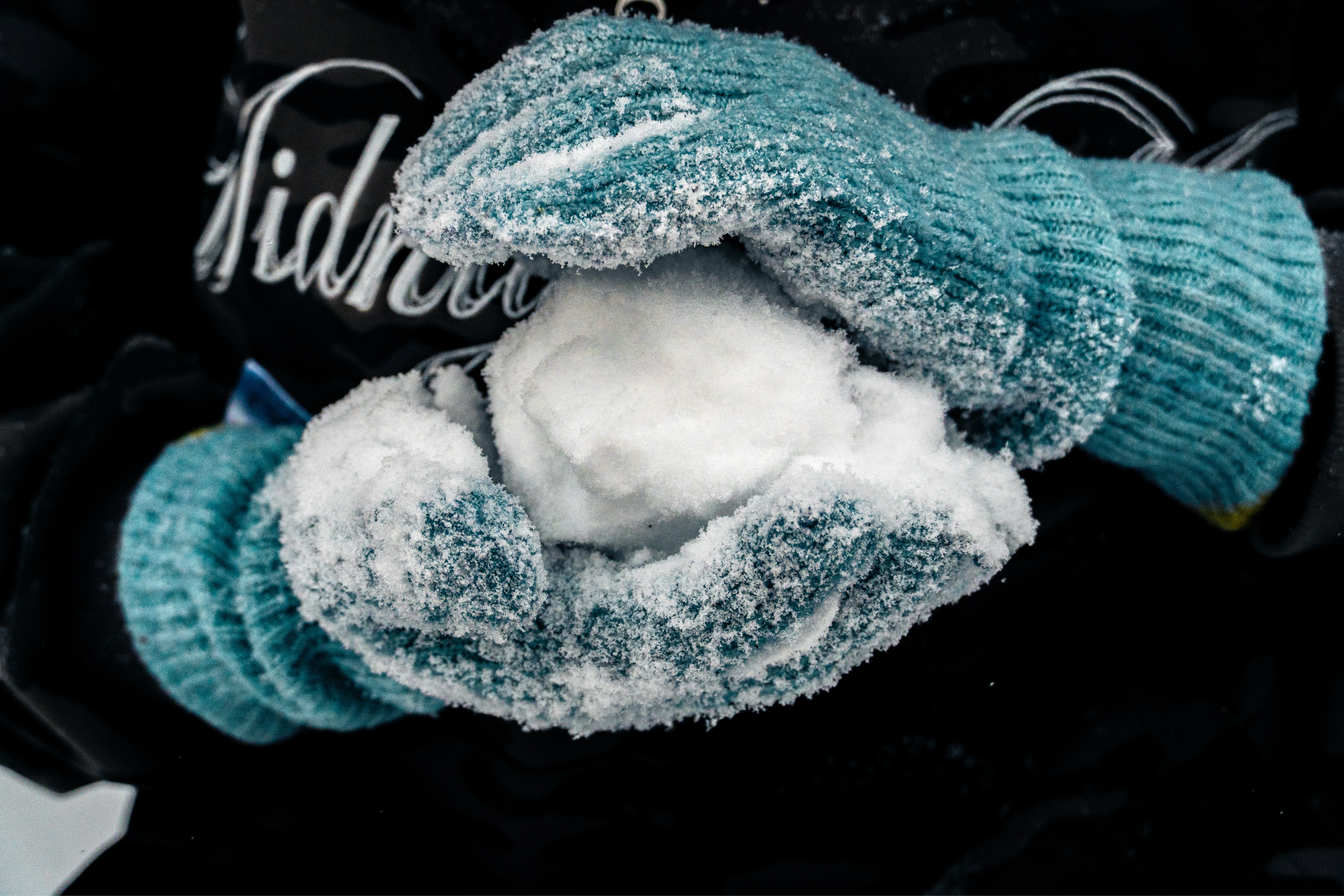 Photo of a blue-gloved hands cradling a snowball, with one hand supporting the bottom of the ball and the other shaping it.