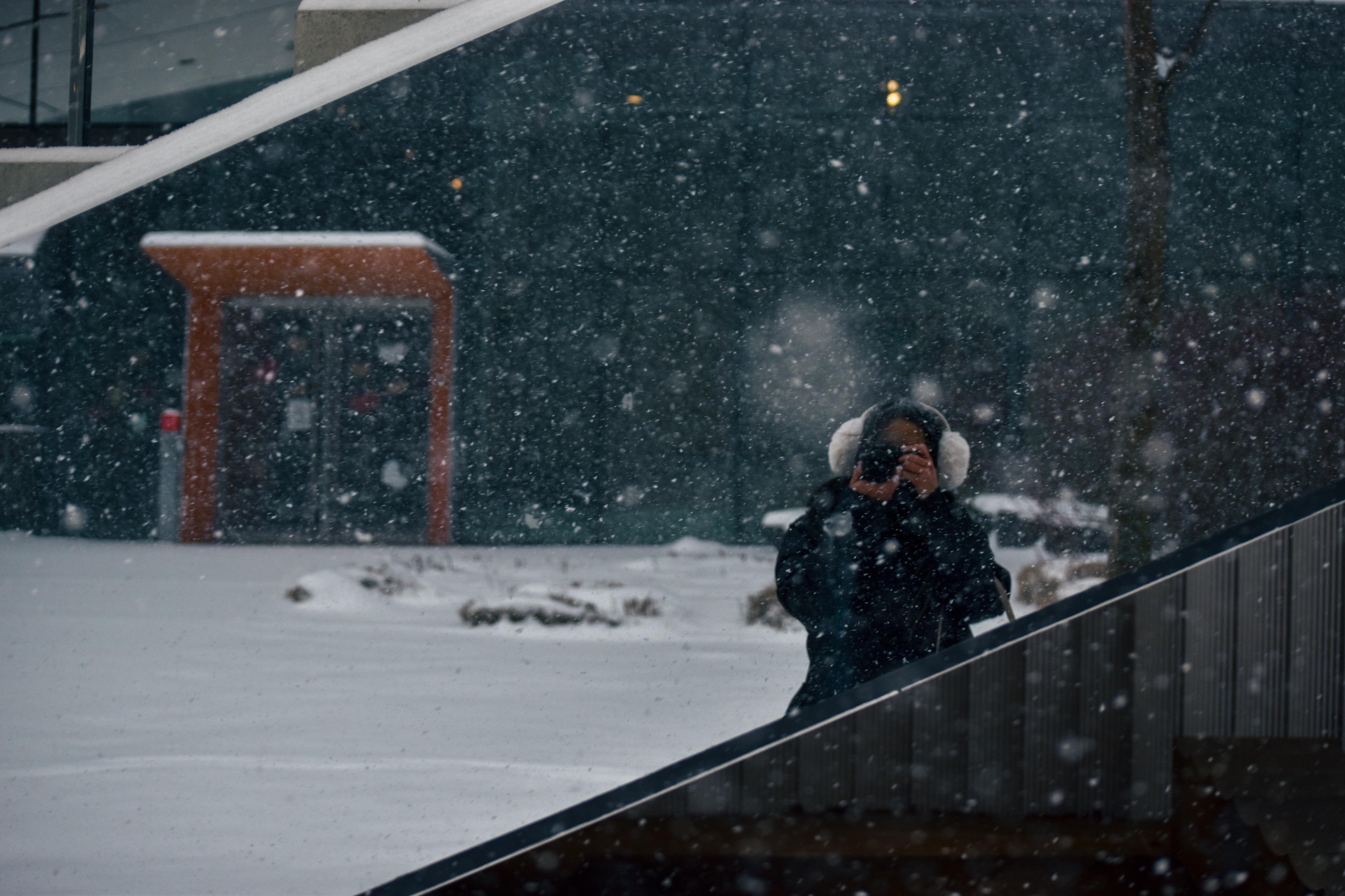 Photo of person with earmuffs taking a photo of falling snow.