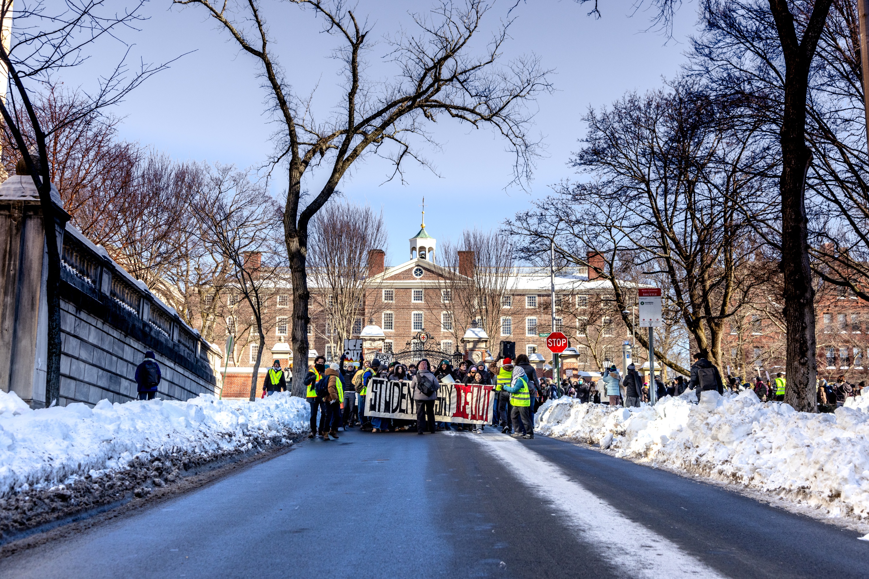 A line of protesters holding a sign titled “STUDENTS SAY ICE OUT” walking down College St.