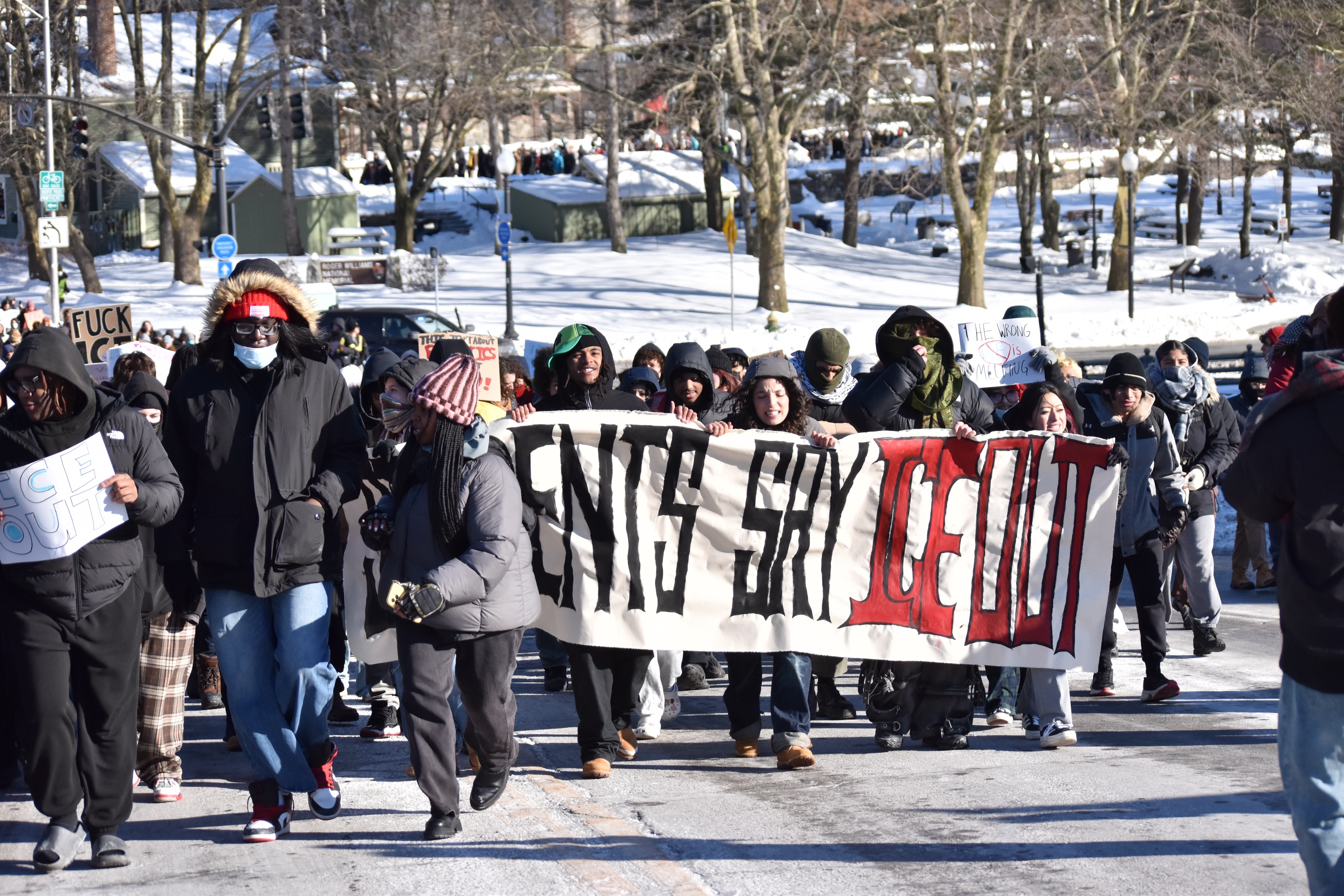 A group of protesters march down a road holding a banner that reads, “Students say ICE out.”