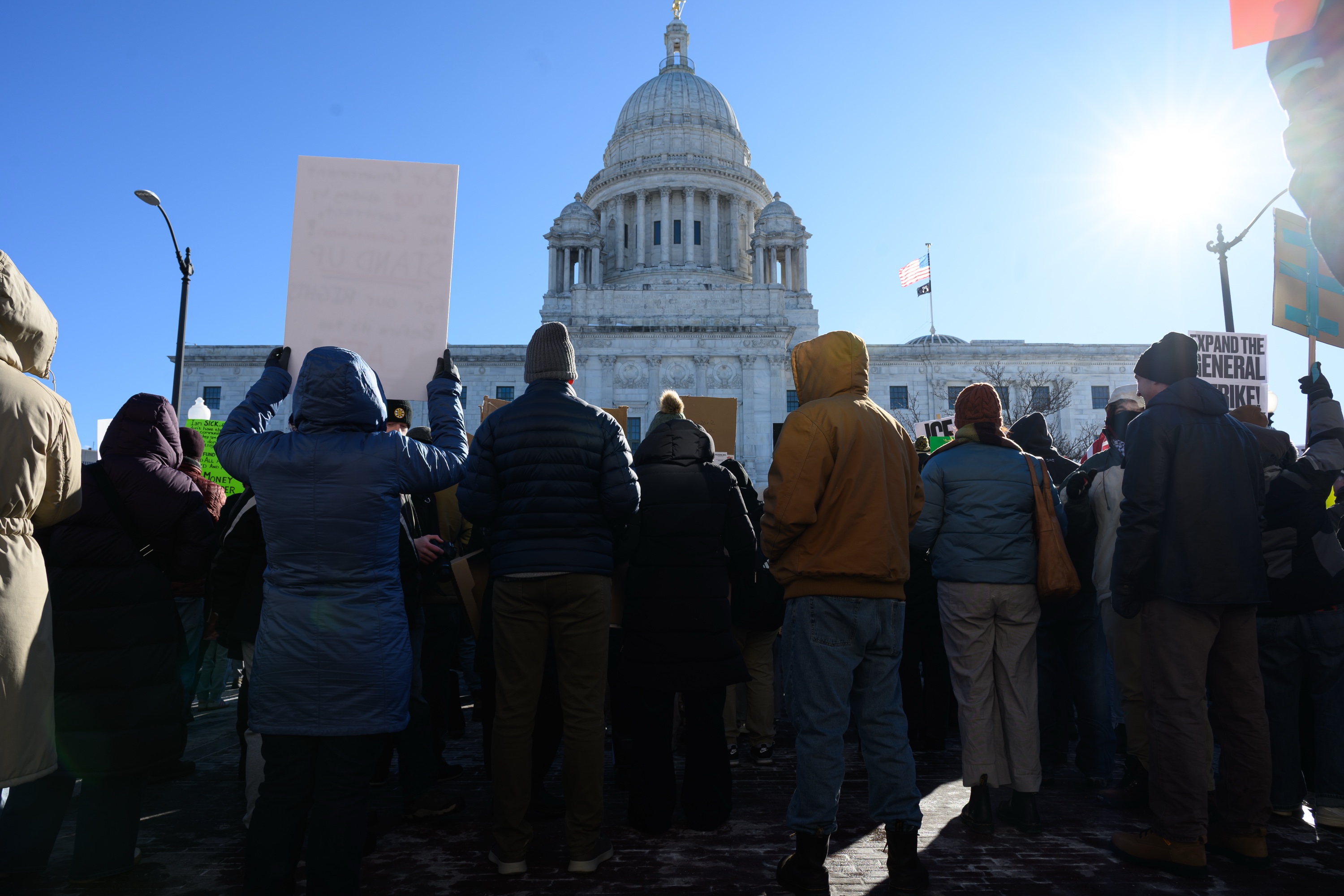 A crowd of protesters cheer in front of the State House.