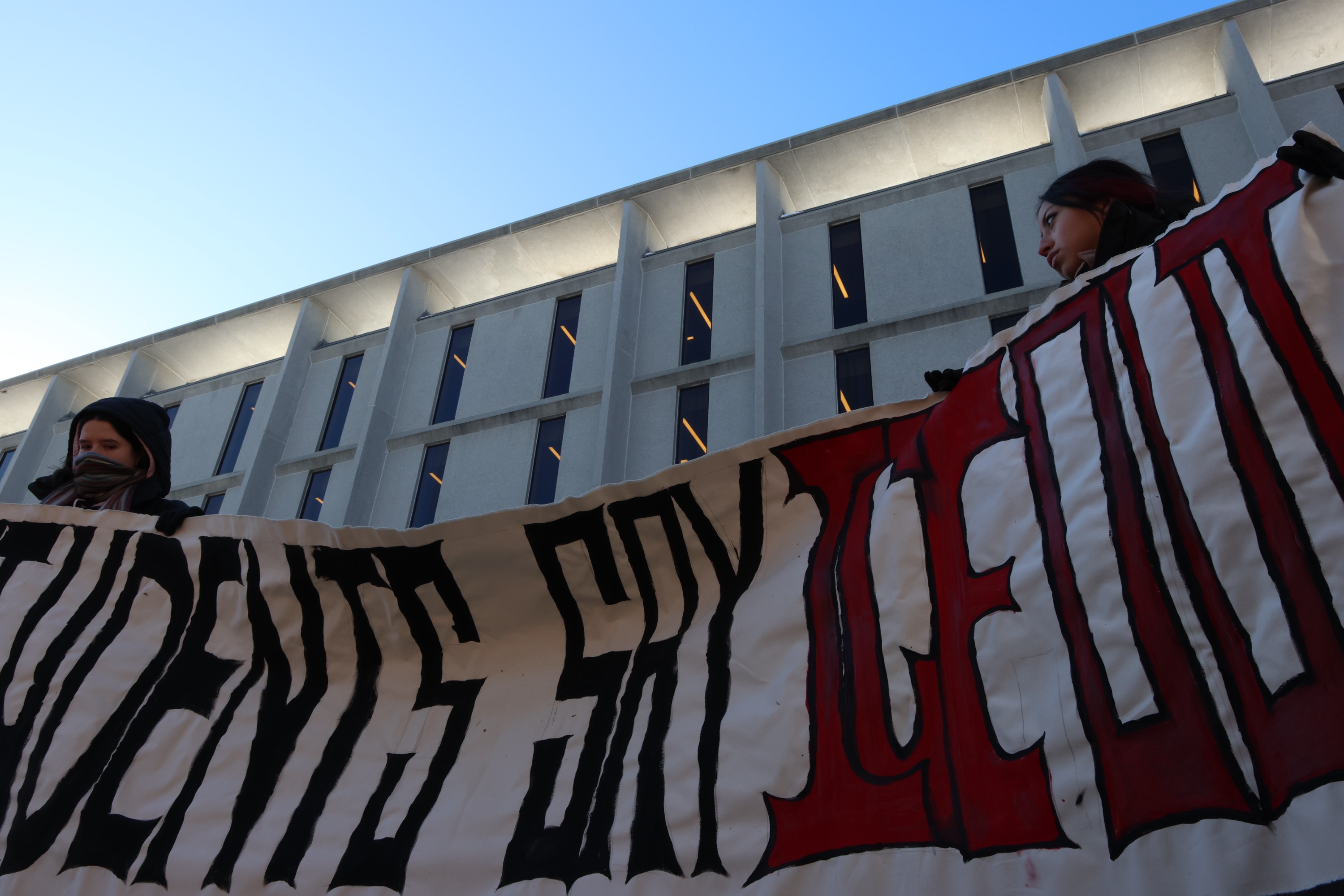 Protesters in front of the John D. Rockefeller Jr. Library holding a cloth banner that states “STUDENTS SAY ICE OUT.”
