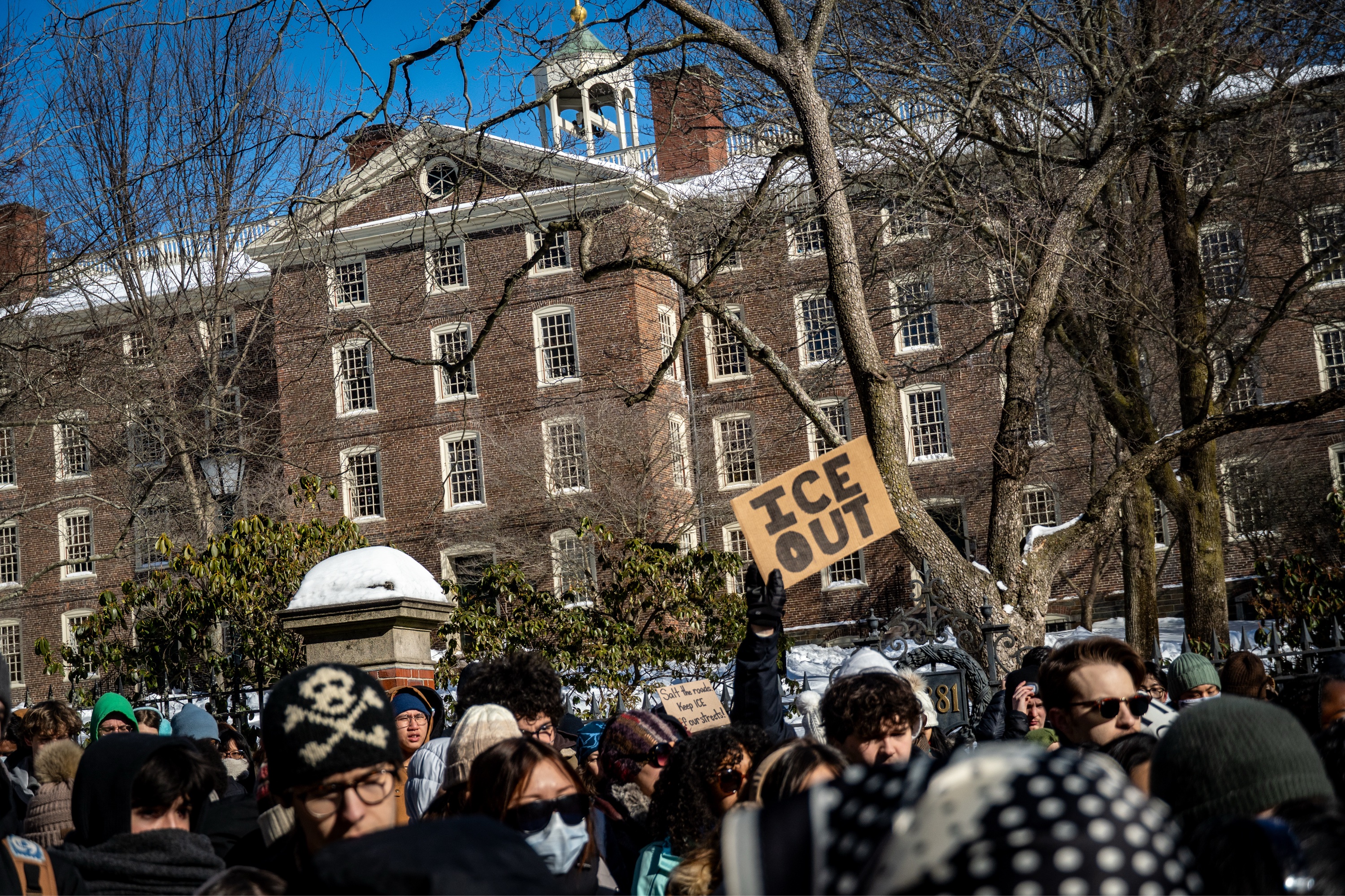 A group of protesters gather outside University Hall. One protester holds up a sign that says, “ICE OUT.”