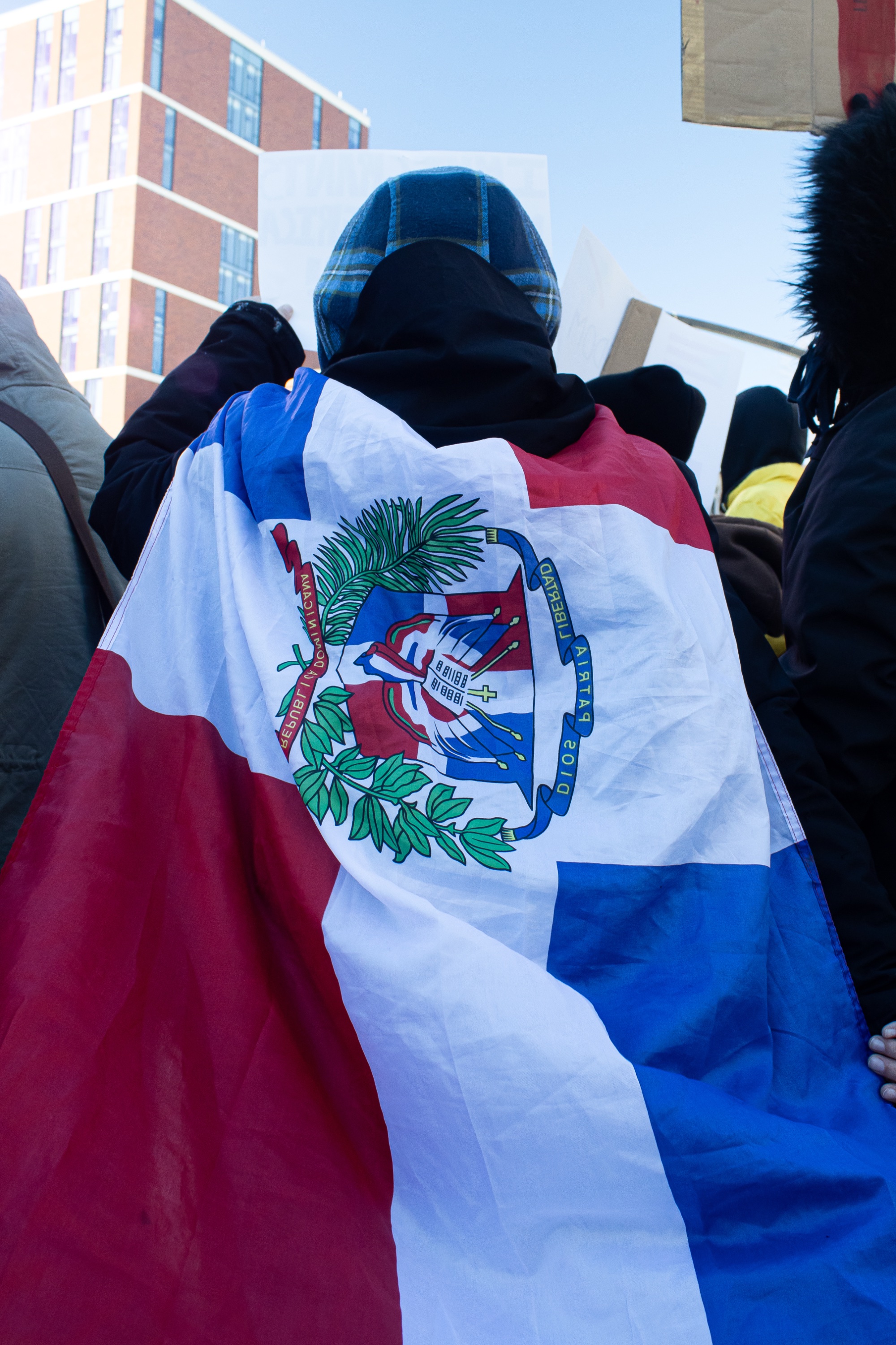 The back of a protester wearing the flag of the Dominican Republic as a cape.