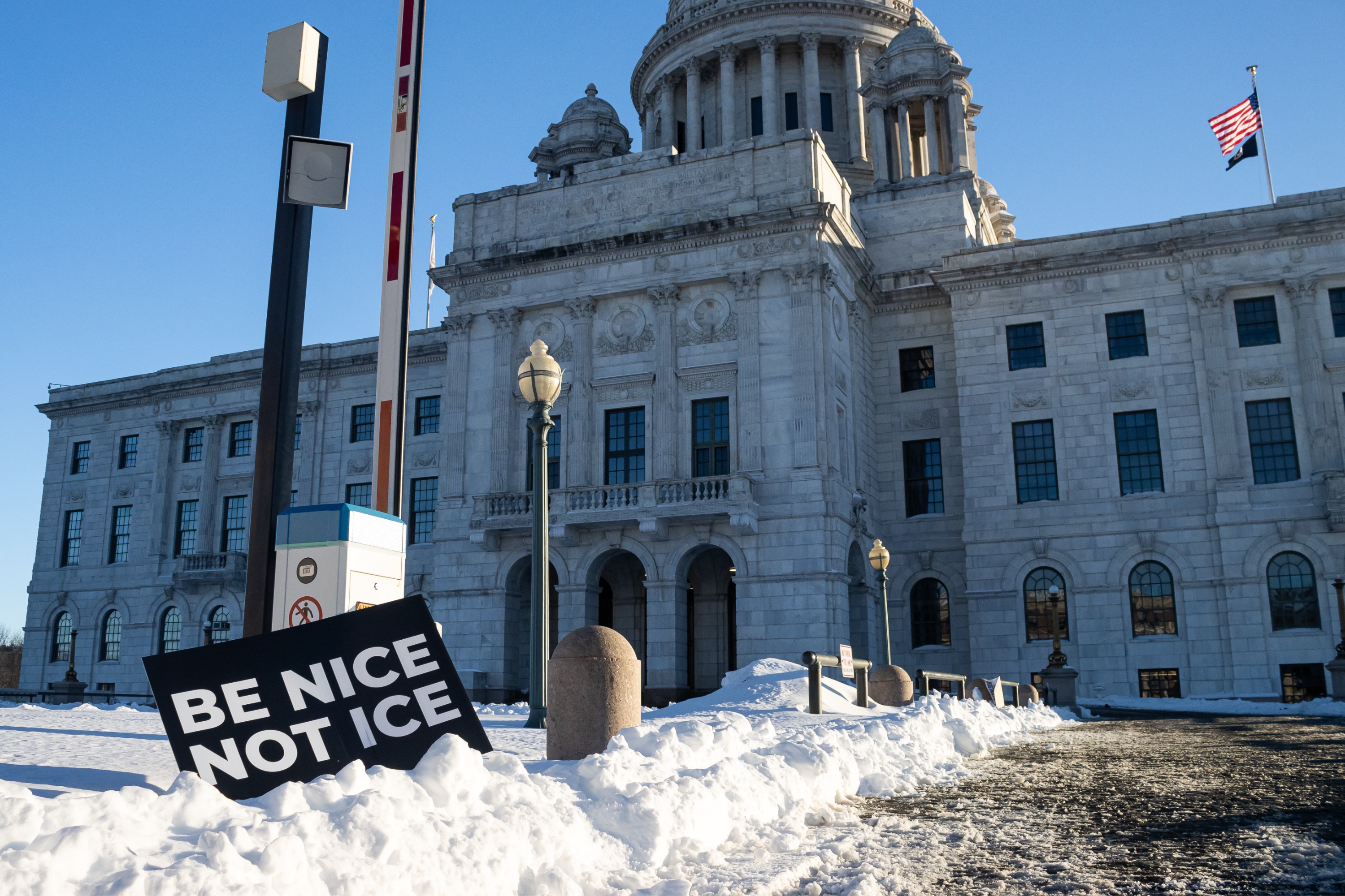 A sign displaying the words “BE NICE / NOT ICE” embedded in snow in front of the Rhode Island State House.